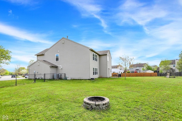 back of house featuring a fire pit, cooling unit, a lawn, and fence