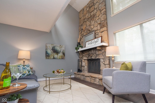 living room featuring wood finished floors, baseboards, a stone fireplace, and lofted ceiling