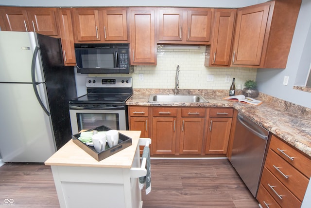 kitchen featuring decorative backsplash, appliances with stainless steel finishes, brown cabinets, a sink, and dark wood-type flooring