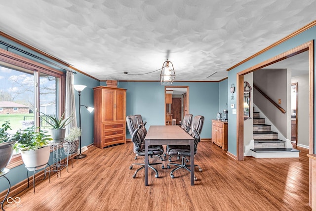 dining area featuring light wood-type flooring, baseboards, ornamental molding, and stairs