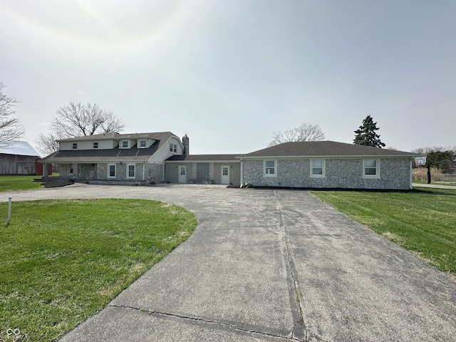 view of front of property featuring a front yard, stone siding, a chimney, and curved driveway