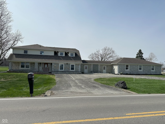 view of front of home with a shingled roof, aphalt driveway, stone siding, and a front lawn