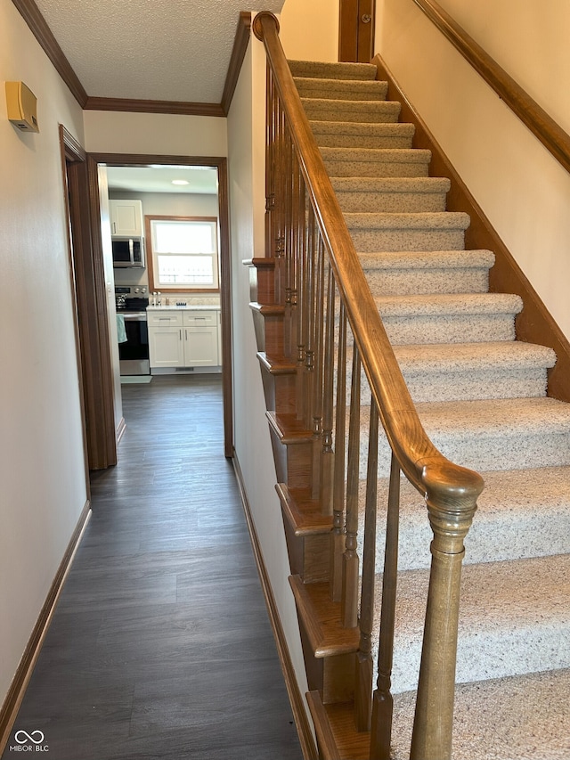 staircase featuring a textured ceiling, wood finished floors, baseboards, and ornamental molding
