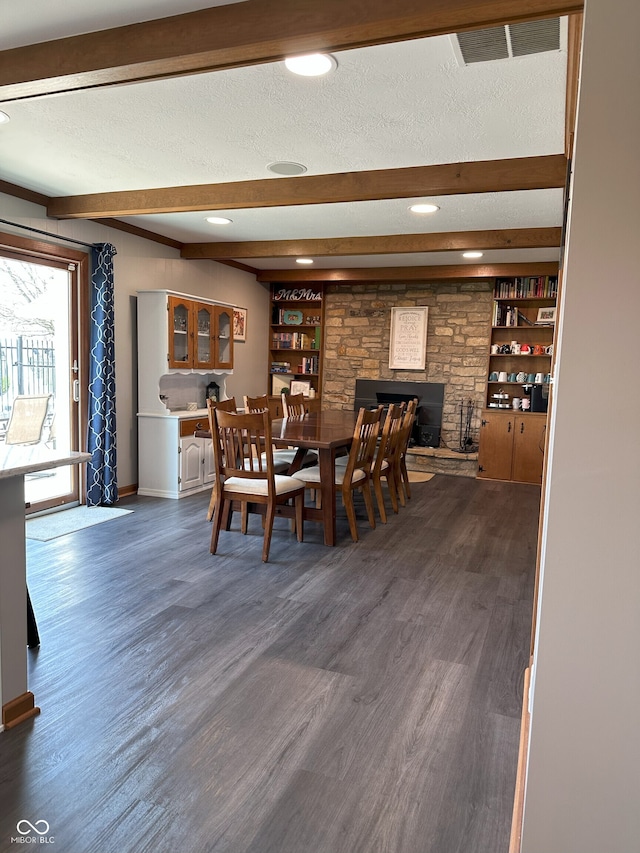 dining room with a textured ceiling, dark wood-style flooring, a fireplace, and beam ceiling