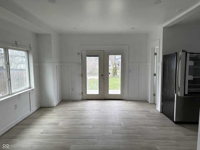 unfurnished dining area featuring a wealth of natural light, light wood-style flooring, and a wainscoted wall
