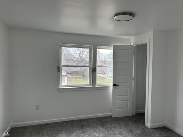 unfurnished room featuring a healthy amount of sunlight, dark colored carpet, and baseboards
