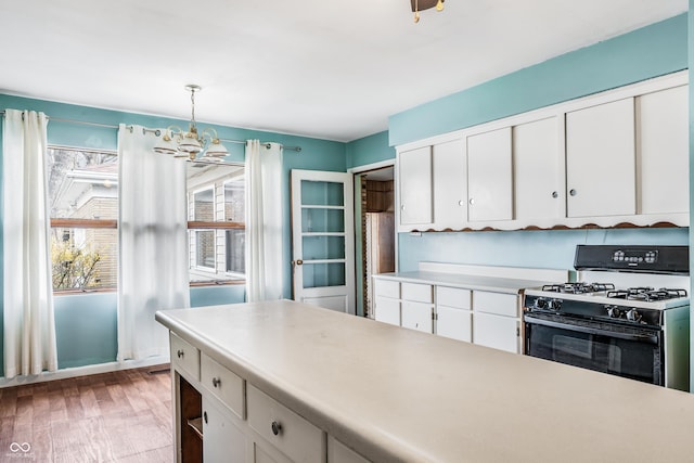kitchen featuring light countertops, gas range oven, a notable chandelier, and white cabinets