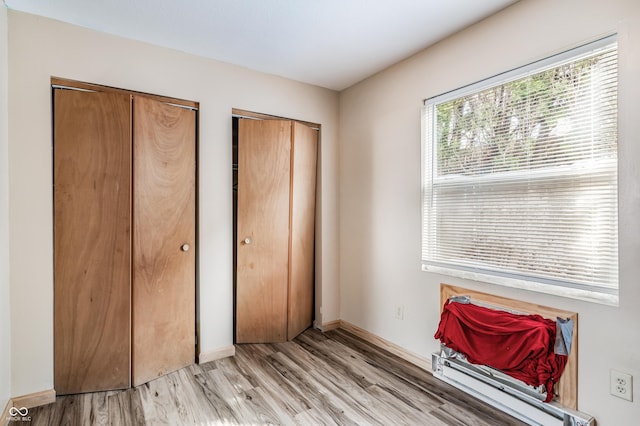 unfurnished bedroom with light wood-style flooring, baseboards, and two closets