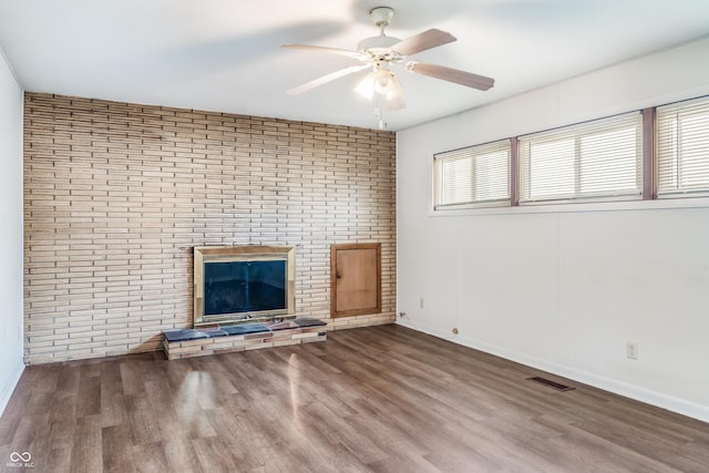 unfurnished living room with a ceiling fan, visible vents, wood finished floors, brick wall, and baseboards