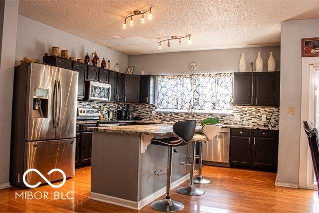 10105 Yosemite Ln, Indianapolis, IN 46234 - kitchen with light wood-type flooring, backsplash, light stone countertops, a kitchen bar, and stainless steel appliances