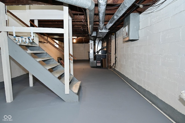 unfinished basement with concrete block wall, heating unit, and stairs