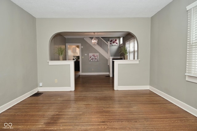 unfurnished room with visible vents, baseboards, arched walkways, and wood finished floors