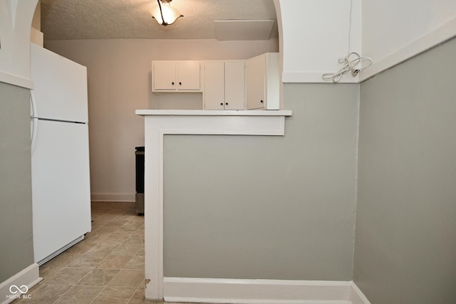 kitchen with white cabinets, baseboards, freestanding refrigerator, and a textured ceiling