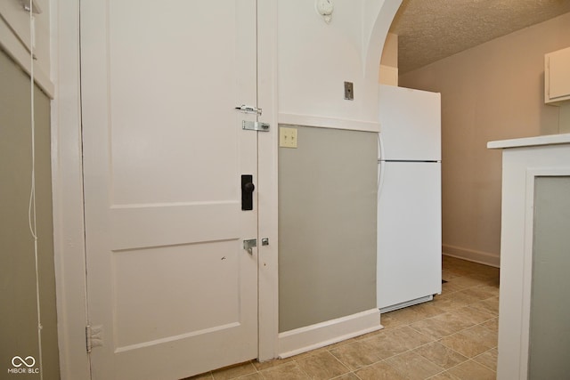 kitchen with freestanding refrigerator, arched walkways, a textured ceiling, white cabinetry, and baseboards