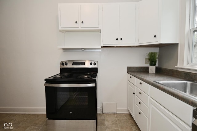 kitchen featuring white cabinets, baseboards, stainless steel range with electric stovetop, a sink, and dark countertops