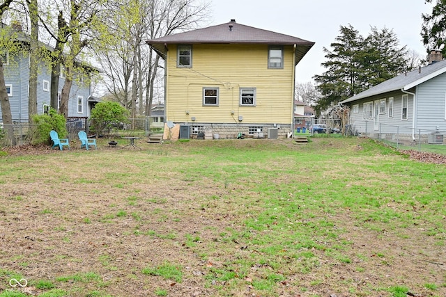 rear view of house with a yard, a fire pit, fence, and central AC unit