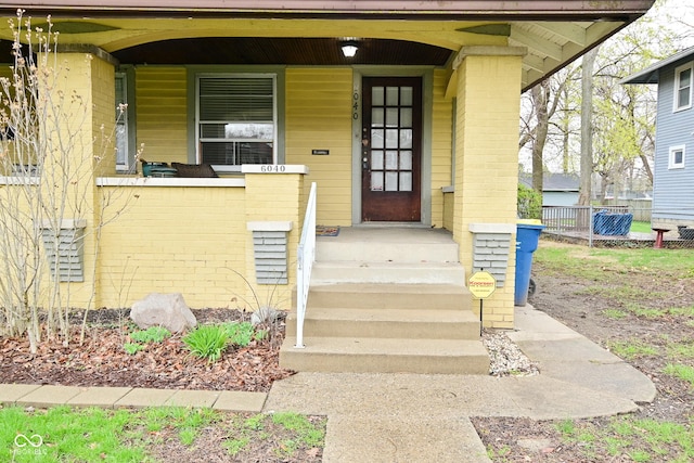 doorway to property featuring brick siding and fence