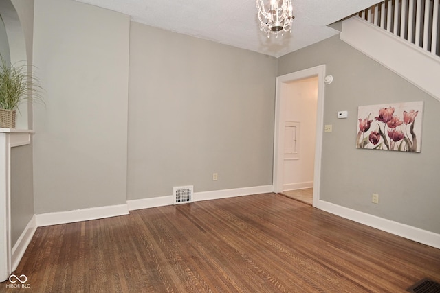 unfurnished room featuring a chandelier, wood finished floors, baseboards, and visible vents