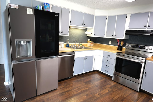 kitchen with light countertops, under cabinet range hood, dark wood finished floors, stainless steel appliances, and a sink