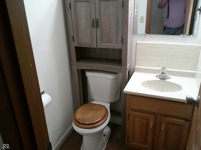 half bath with toilet, vanity, decorative backsplash, and baseboards