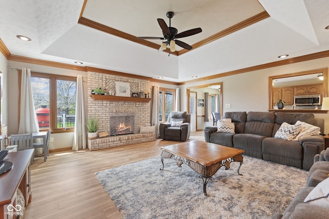 8095 Christopher Ct, Avon, IN 46123 - living area featuring a tray ceiling, light wood-style floors, a brick fireplace, ceiling fan, and crown molding