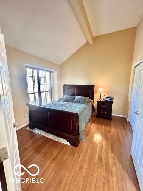 bedroom featuring light wood-style flooring, baseboards, and vaulted ceiling with beams