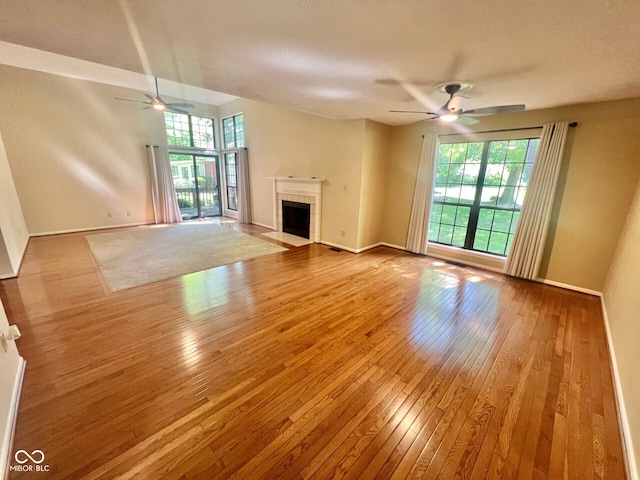 unfurnished living room with a tiled fireplace, wood-type flooring, baseboards, and a ceiling fan