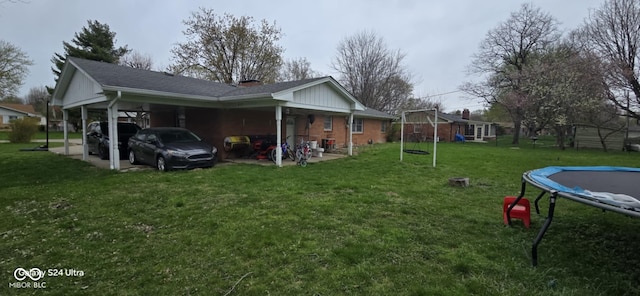 rear view of house with a carport, a trampoline, and a yard