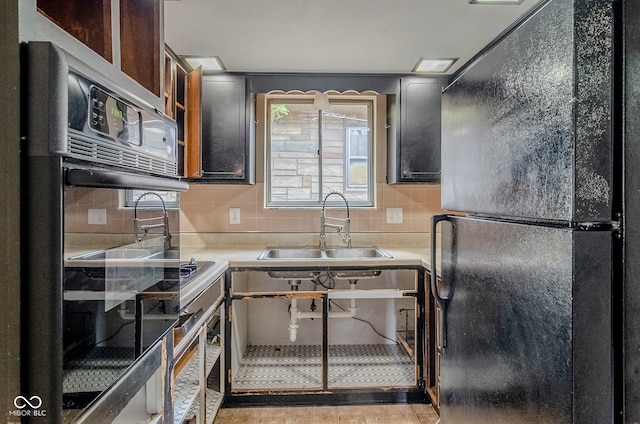 kitchen with light countertops, decorative backsplash, a sink, and black appliances
