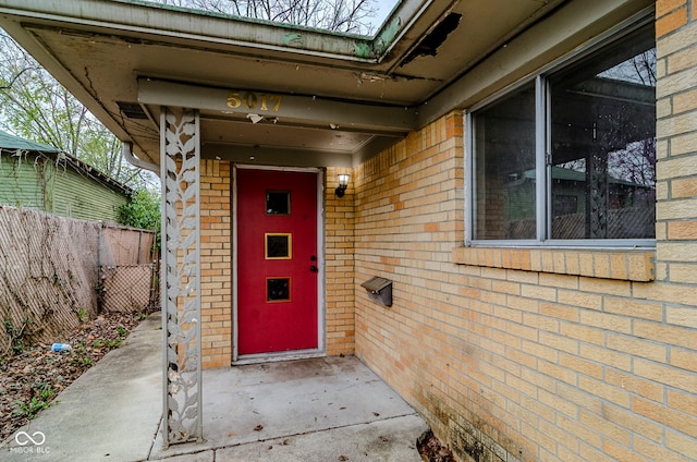 view of exterior entry featuring fence, brick siding, and a patio