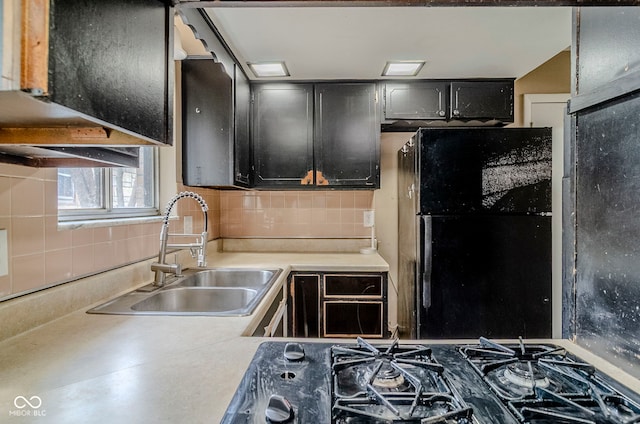 kitchen featuring a sink, freestanding refrigerator, dark cabinetry, decorative backsplash, and light countertops