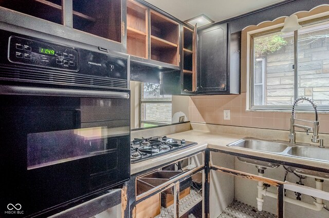 kitchen featuring a sink, tasteful backsplash, glass insert cabinets, light countertops, and black oven