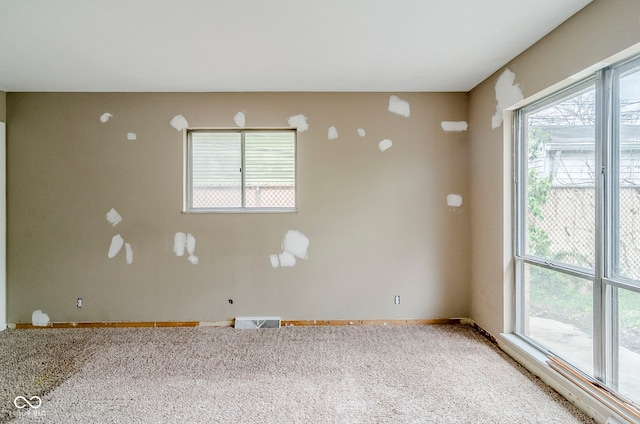 carpeted spare room with a wealth of natural light, baseboards, and visible vents