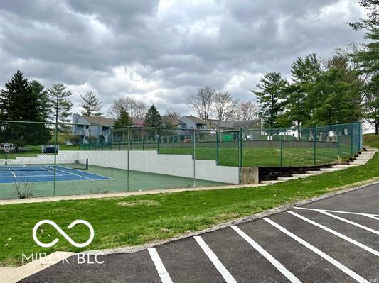 view of community featuring a yard, a tennis court, and fence