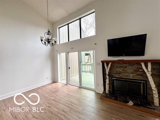 unfurnished living room with a stone fireplace, baseboards, a chandelier, high vaulted ceiling, and wood finished floors