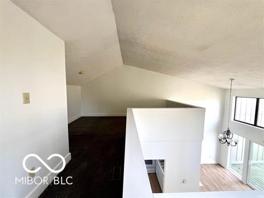 bonus room featuring a notable chandelier, a textured ceiling, baseboards, and lofted ceiling
