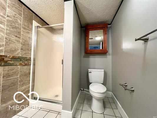 full bath featuring a textured ceiling, tile patterned flooring, toilet, a stall shower, and baseboards