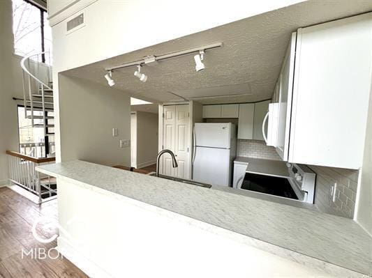 kitchen featuring white appliances, track lighting, a peninsula, a sink, and backsplash