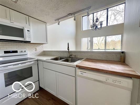 kitchen with track lighting, a sink, white appliances, a textured ceiling, and butcher block counters