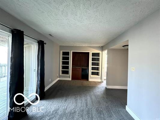 spare room with built in features, baseboards, dark colored carpet, and a textured ceiling