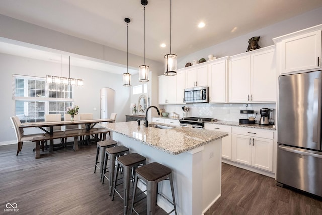 1534 Cloverdon Dr, Westfield, IN 46074 - kitchen with stainless steel appliances, a sink, a kitchen island with sink, dark wood-style floors, and arched walkways