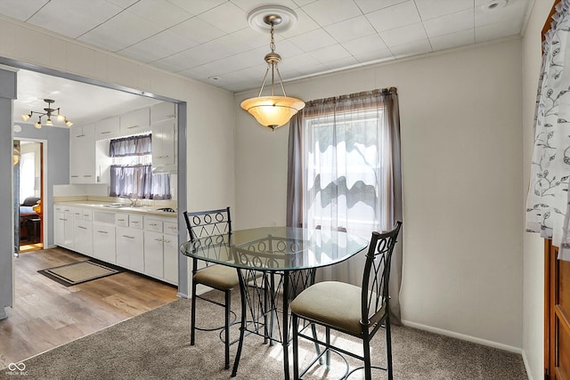 dining room with light carpet, a chandelier, and baseboards