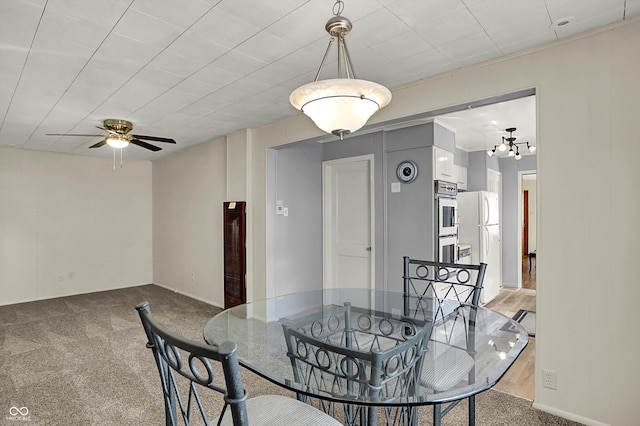 carpeted dining room with ceiling fan and a chandelier