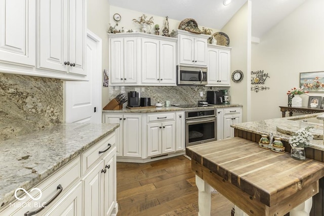 kitchen featuring appliances with stainless steel finishes, dark wood finished floors, white cabinetry, vaulted ceiling, and backsplash