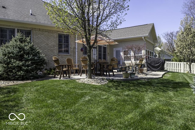 back of property featuring a yard, a patio area, fence, brick siding, and roof with shingles