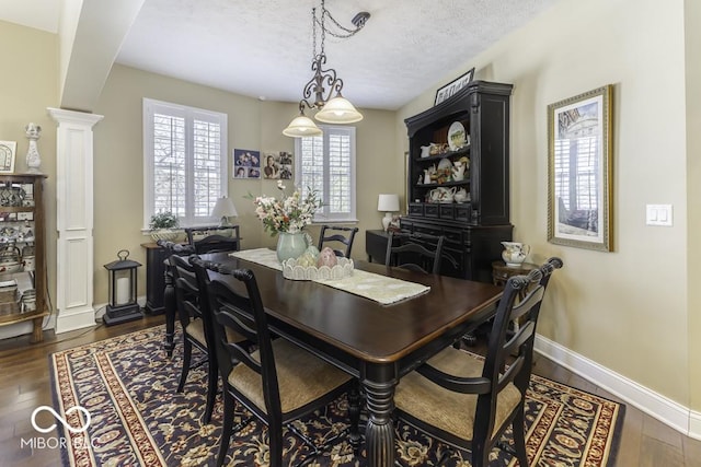 dining area featuring a textured ceiling, ornate columns, baseboards, and dark wood finished floors