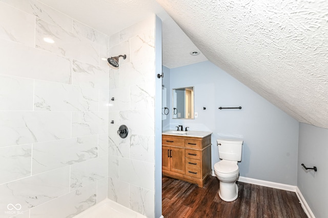 bathroom with a textured ceiling, tiled shower, vanity, toilet, and wood finished floors