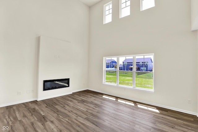 3727 Thomas Jefferson Ct, Westfield, IN 46074 - unfurnished living room featuring a towering ceiling, wood finished floors, a glass covered fireplace, and baseboards