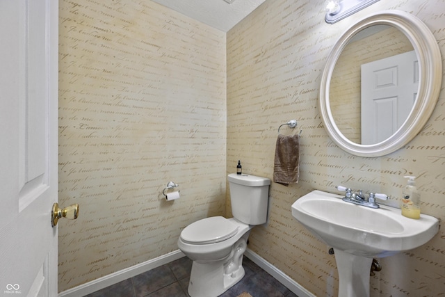 half bathroom with toilet, a sink, baseboards, and tile patterned flooring