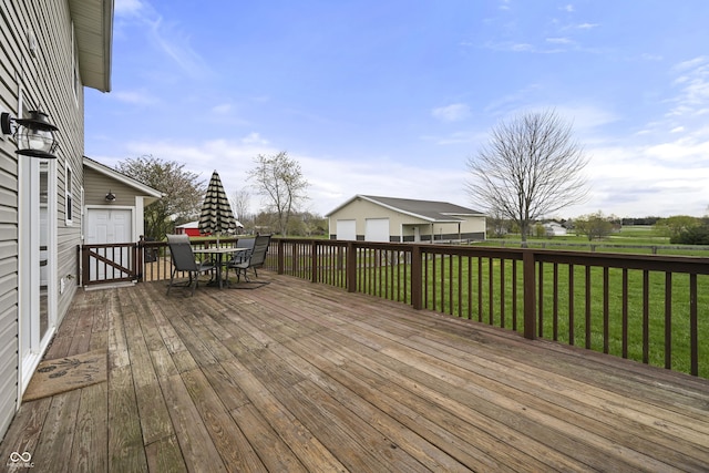 deck featuring outdoor dining space, a garage, an outdoor structure, and a lawn